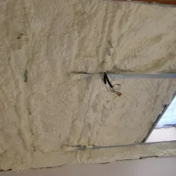 Poddasze po natrysku pianki poliuretanowej, widoczne metalowe profile, przewody elektryczne i okno dachowe.