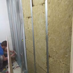 Jaśko - Montaż izolacji z wełny mineralnej w metalowym stelażu pod płytę karton-gips, widoczne narzędzia i poziomica.