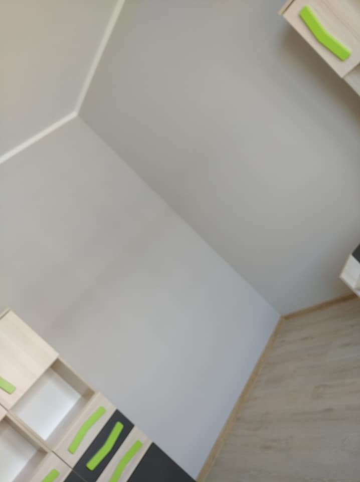 Fragment pokoju po odświeżeniu, z widoczną ścianą pomalowaną na szaro i zamontowanymi meblami z jasnego drewna z zielonymi akcentami, oraz podłogą w kolorze naturalnego drewna.