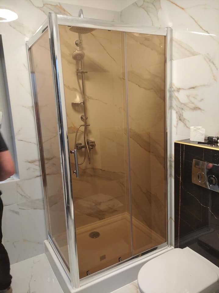 Zmontowana kabina prysznicowa z brązowymi szybami i srebrnymi profilami w łazience z marmurowymi płytkami, widoczny panel sterowania prysznicem i toaleta.