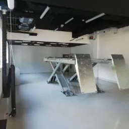 Warsztat samochodowy z podnośnikiem dwukolumnowym, systemem wentylacji i oświetleniem LED, widok z boku na puste stanowisko pracy.