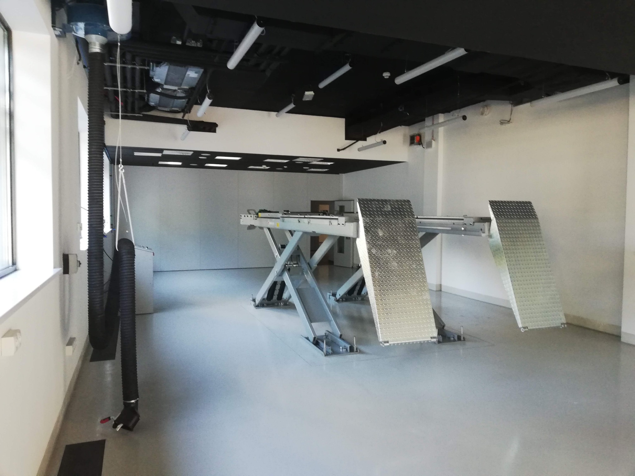 Warsztat samochodowy z podnośnikiem dwukolumnowym, systemem wentylacji i oświetleniem LED, widok z boku na puste stanowisko pracy.