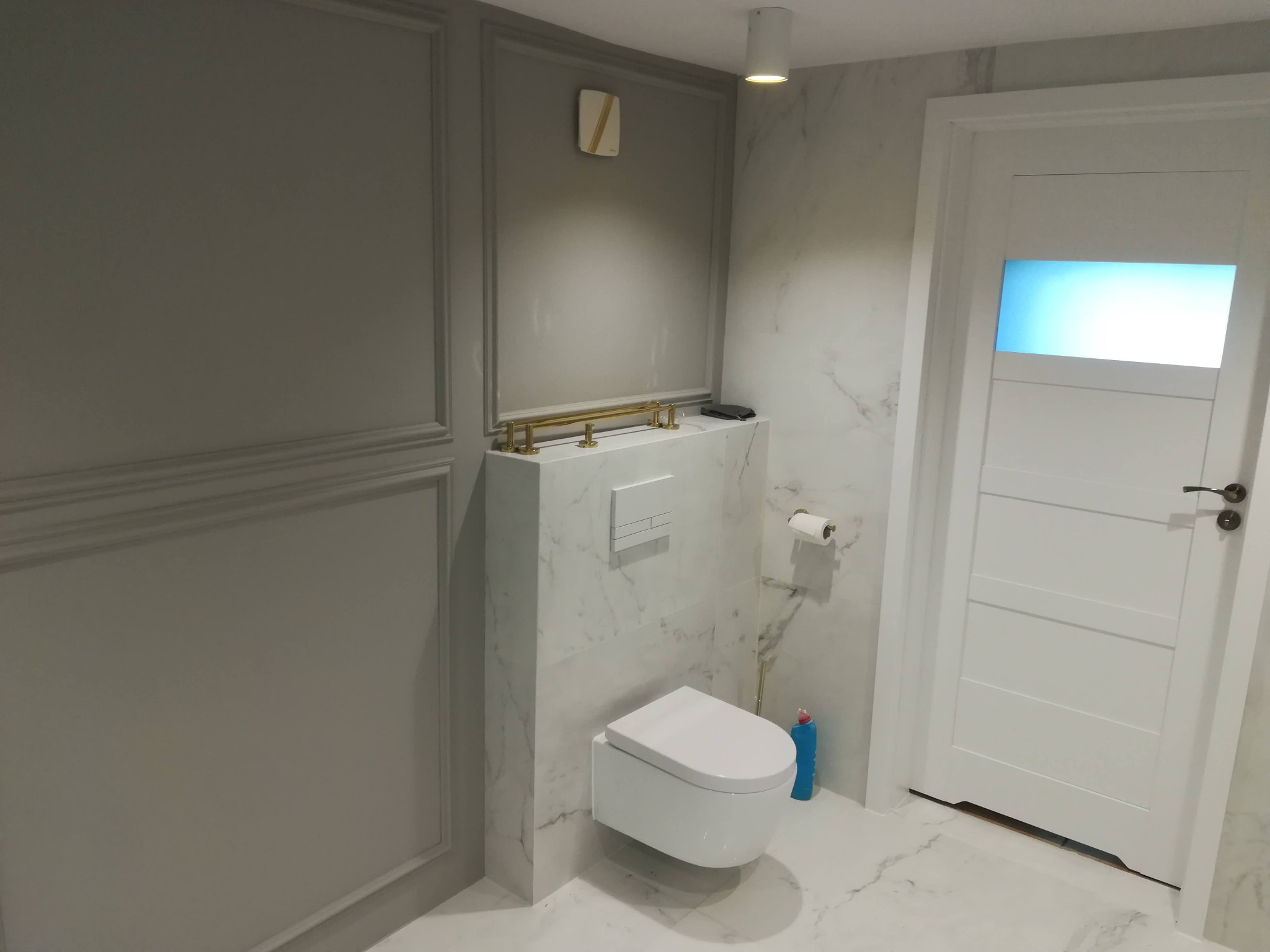 Nowoczesna łazienka w Łomży z podtynkową toaletą, marmurowymi płytkami i szarą ścianą z dekoracyjnymi listwami.