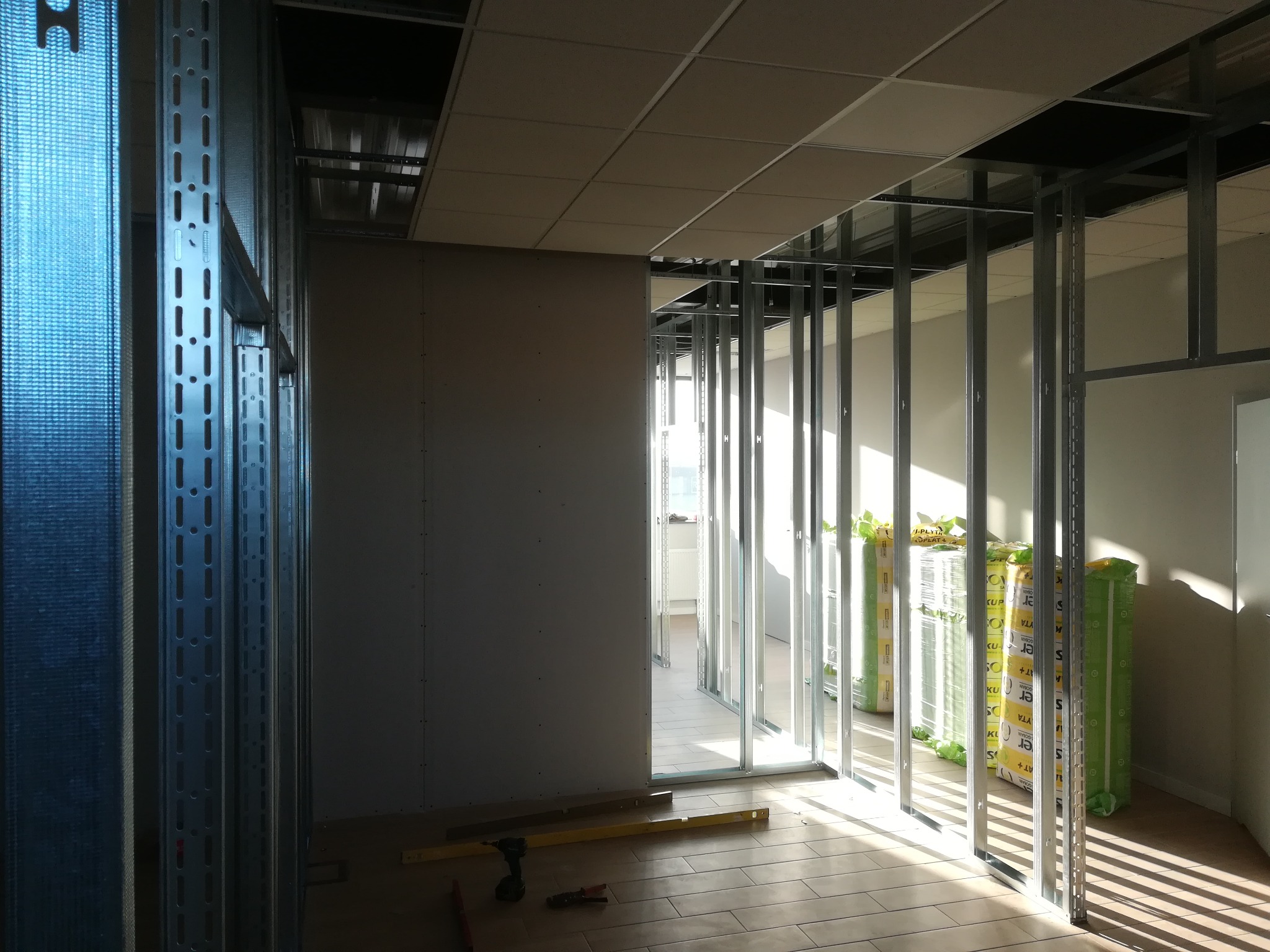 Wnętrze w trakcie montażu ścian działowych z płyt kartonowo-gipsowych na metalowym stelażu, widoczne narzędzia i materiały izolacyjne w folii.