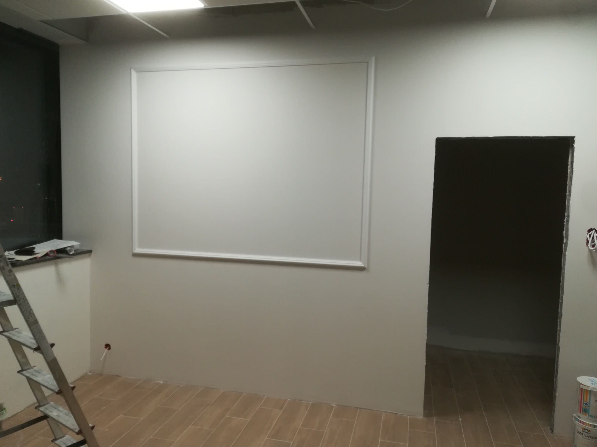 Świeżo pomalowane wnętrze z zamontowaną płytą kartonowo-gipsową tworzącą ozdobną ramę na ścianie, widoczna drabina i puszki z farbą.