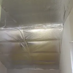 Poddasze z izolacją termiczną pokrytą folią aluminiową, widoczne łączenia i faktura materiału, przygotowane do dalszych prac wykończeniowych.