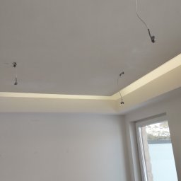 DSfinish - Wnętrze w trakcie wykończenia: sufit z zamontowanym oświetleniem LED, wystające kable, ściany przygotowane do malowania, widoczne okno.