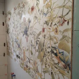 Ściana wyłożona płytkami z motywem kwiatowym i papugami, widoczne otwory na instalację hydrauliczną i małe krzyżyki dystansowe między płytkami.