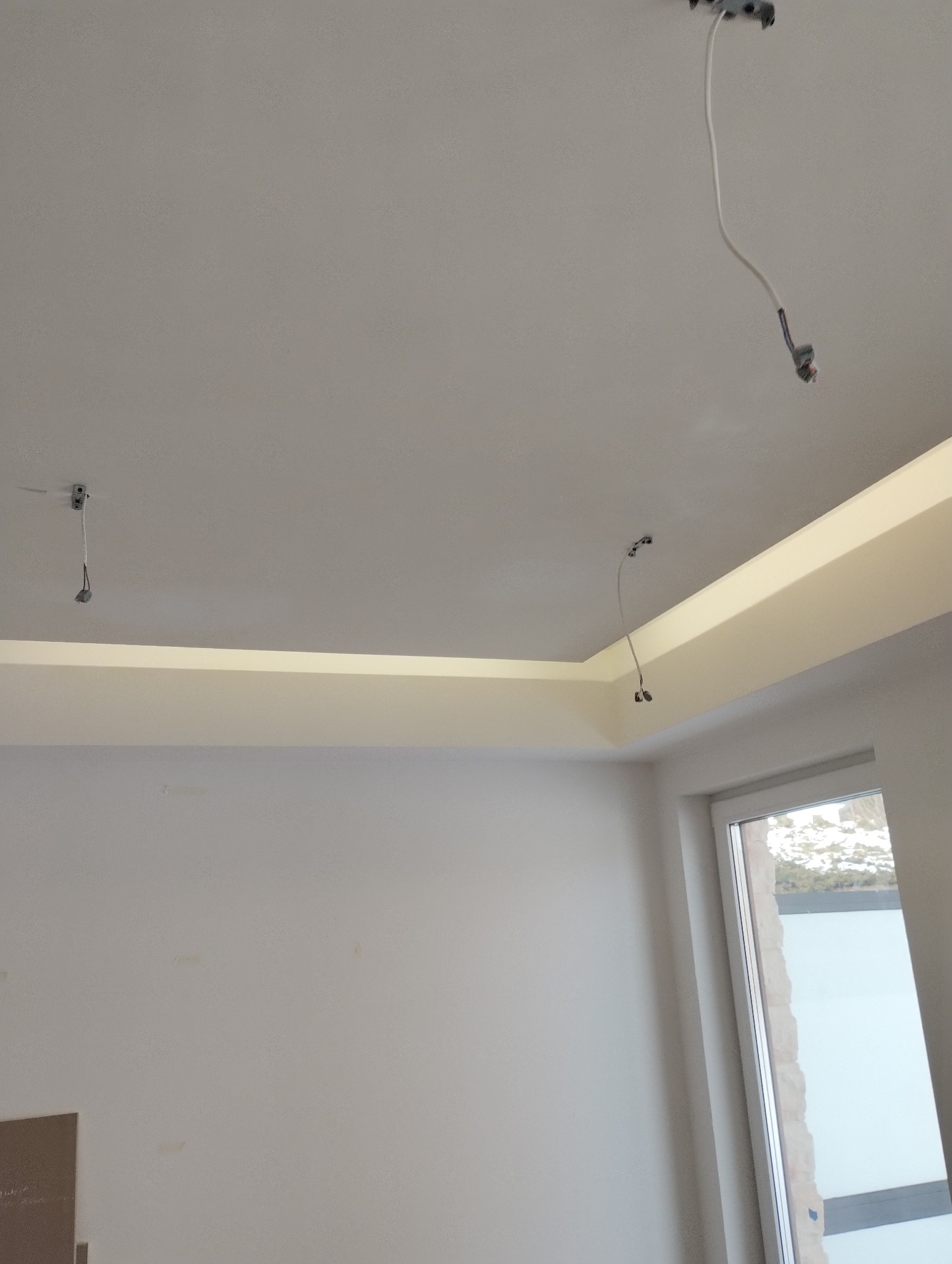 Wnętrze w trakcie wykończenia: sufit z zamontowanym oświetleniem LED, wystające kable, ściany przygotowane do malowania, widoczne okno.