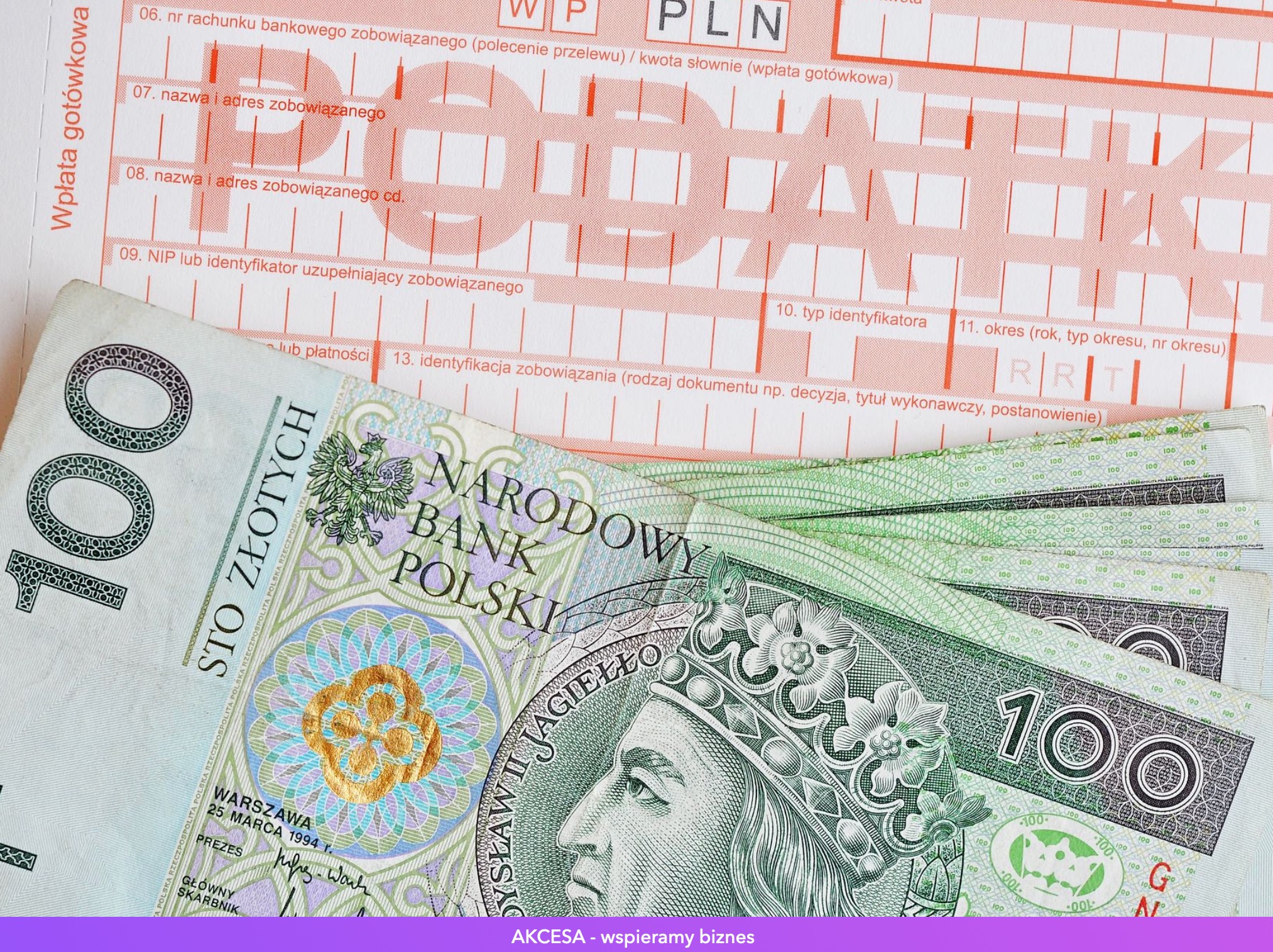 Stos banknotów 100 zł leżący na wypełnionym druku wpłaty gotówkowej z widocznymi polami NIP, adres zobowiązanego i kwota.