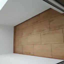 Ściana wyłożona panelami imitującymi drewno, białe ściany i sufit, widok z narożnika pomieszczenia.