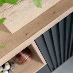 Fragment nowoczesnej zabudowy meblowej z blatem drewnianym, ryflowanymi frontami w kolorze grafitowym i otwartą półką z dekoracjami.