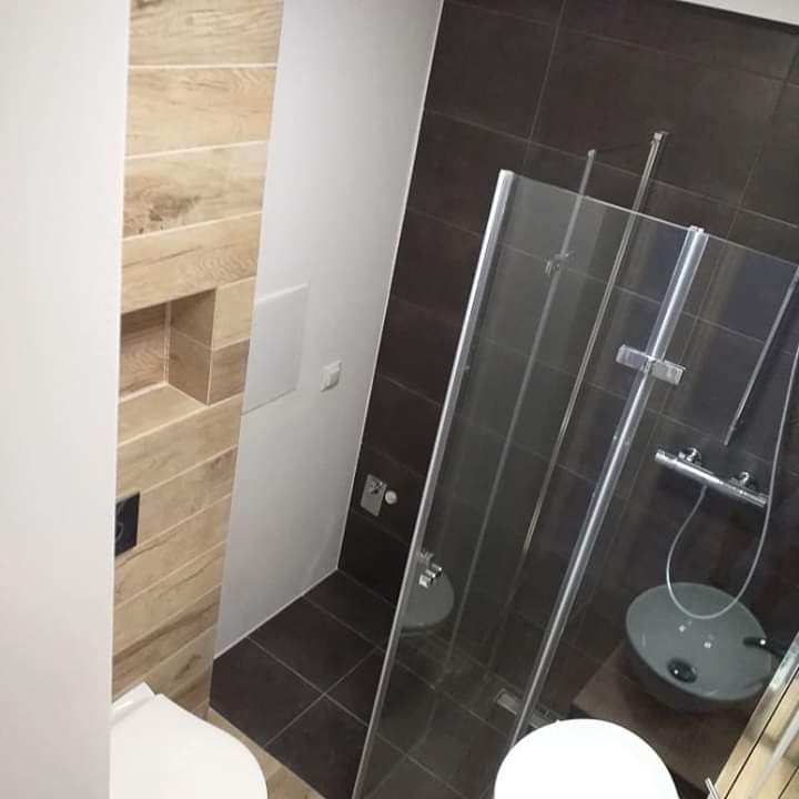 Nowoczesna łazienka z kabiną prysznicową ze szklanymi drzwiami, brązowymi płytkami i drewnopodobną ścianą z wnęką.