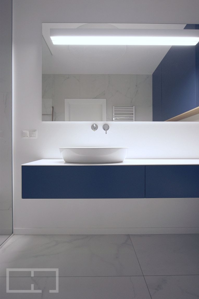 Nowoczesna łazienka z owalną umywalką nablatową, szafką w kolorze granatowym i podświetlanym lustrem, wykończona marmurowymi płytkami.