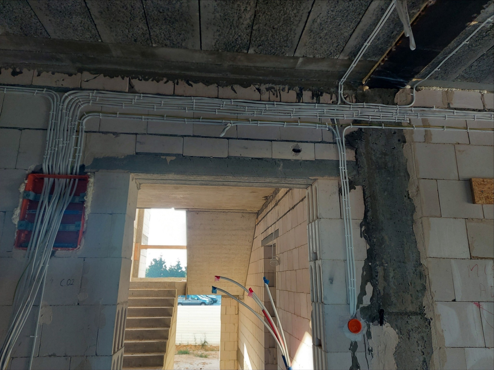 Wewnętrzne rozprowadzenie przewodów elektrycznych w rurkach PCV, widoczne puszki instalacyjne w surowym stanie budynku z bloczków betonowych.