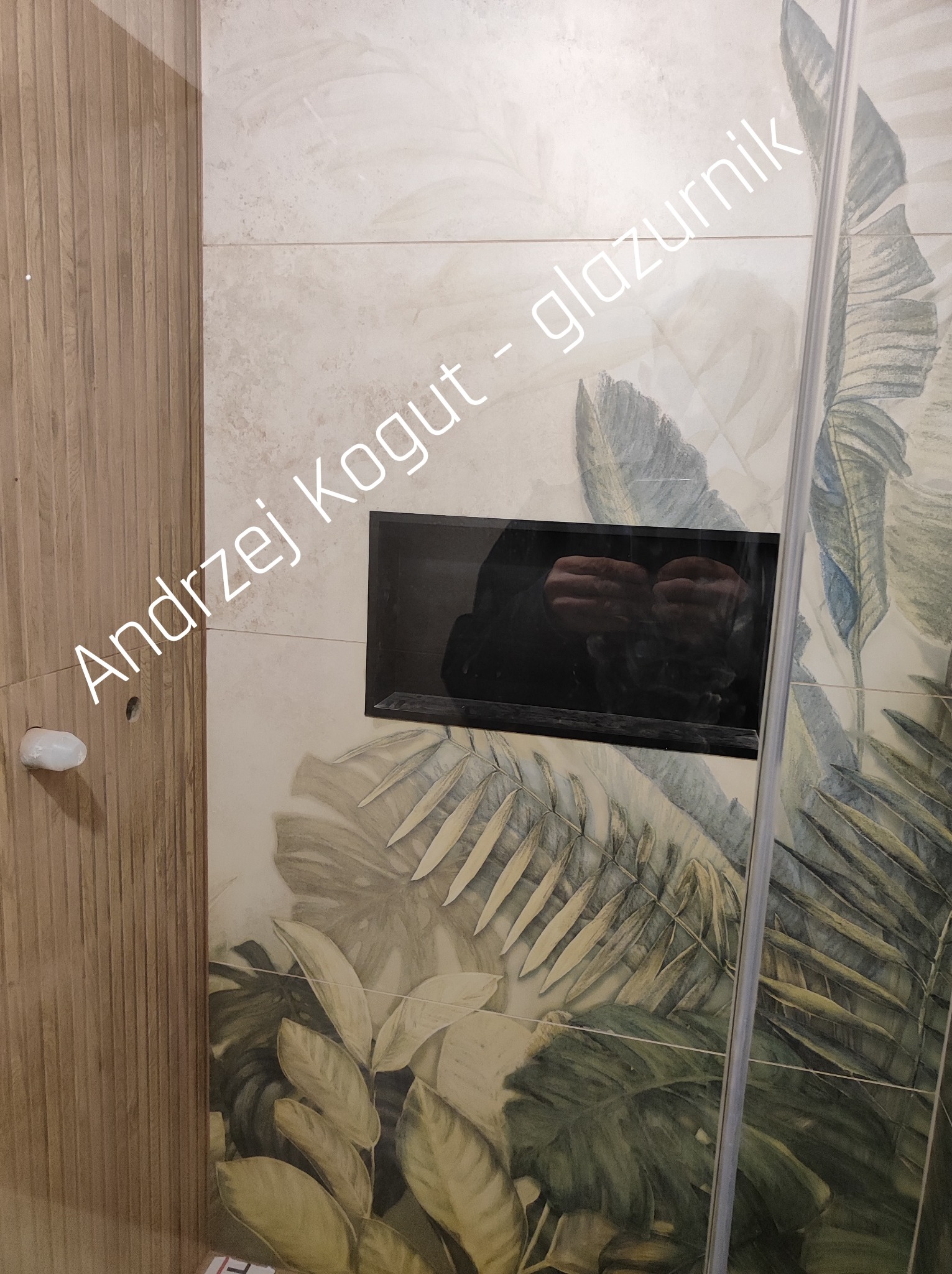 Wykończona ściana łazienki z płytek w tropikalne wzory, z wnęką. Widoczna armatura i fragment kabiny prysznicowej. Ujęcie z bliska, prezentujące detale wykończenia.