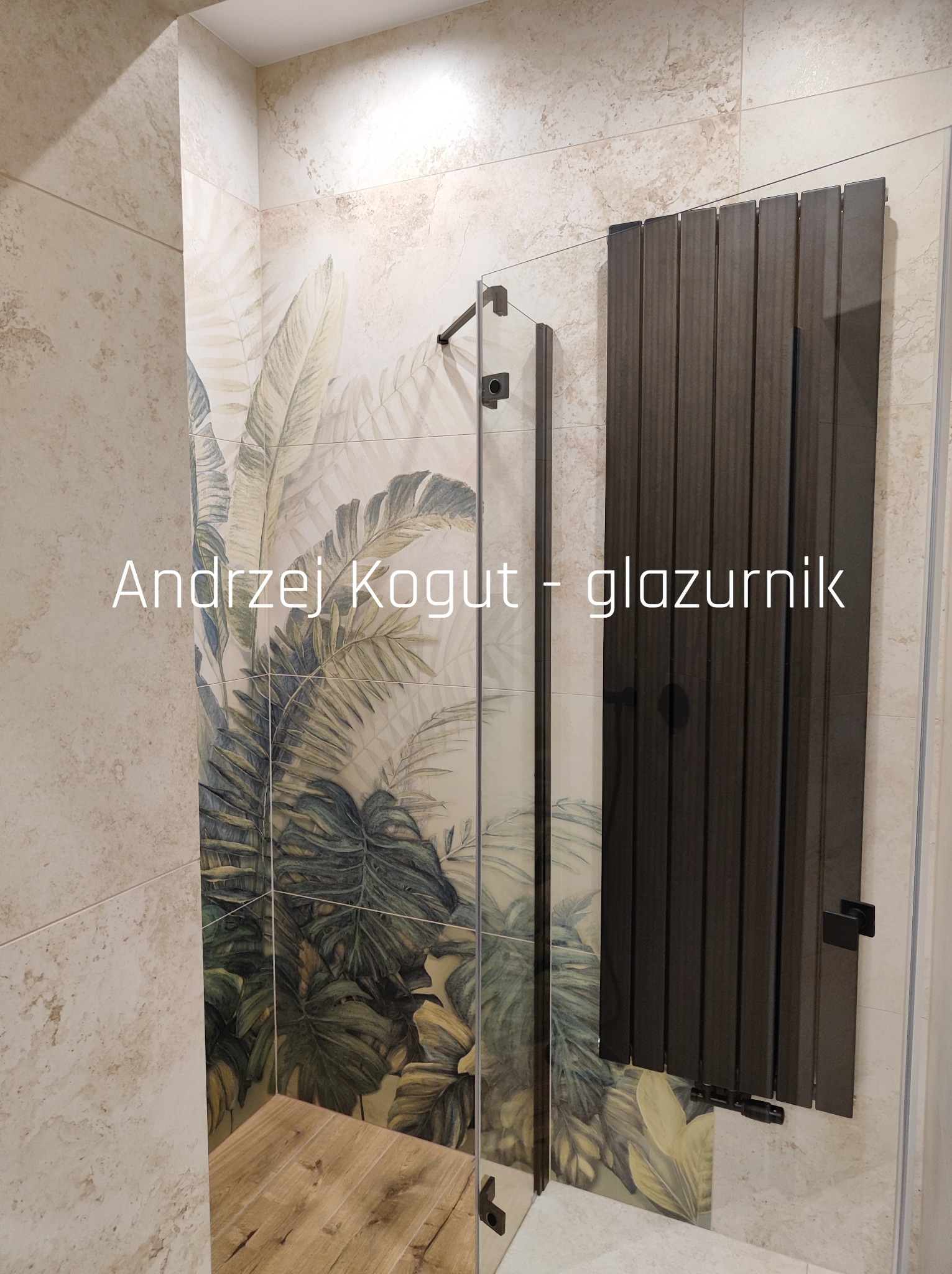 Wykończona łazienka z kabiną prysznicową i grzejnikiem drabinkowym na tle płytek z motywem roślinnym. Widoczny fragment drewnopodobnej podłogi.