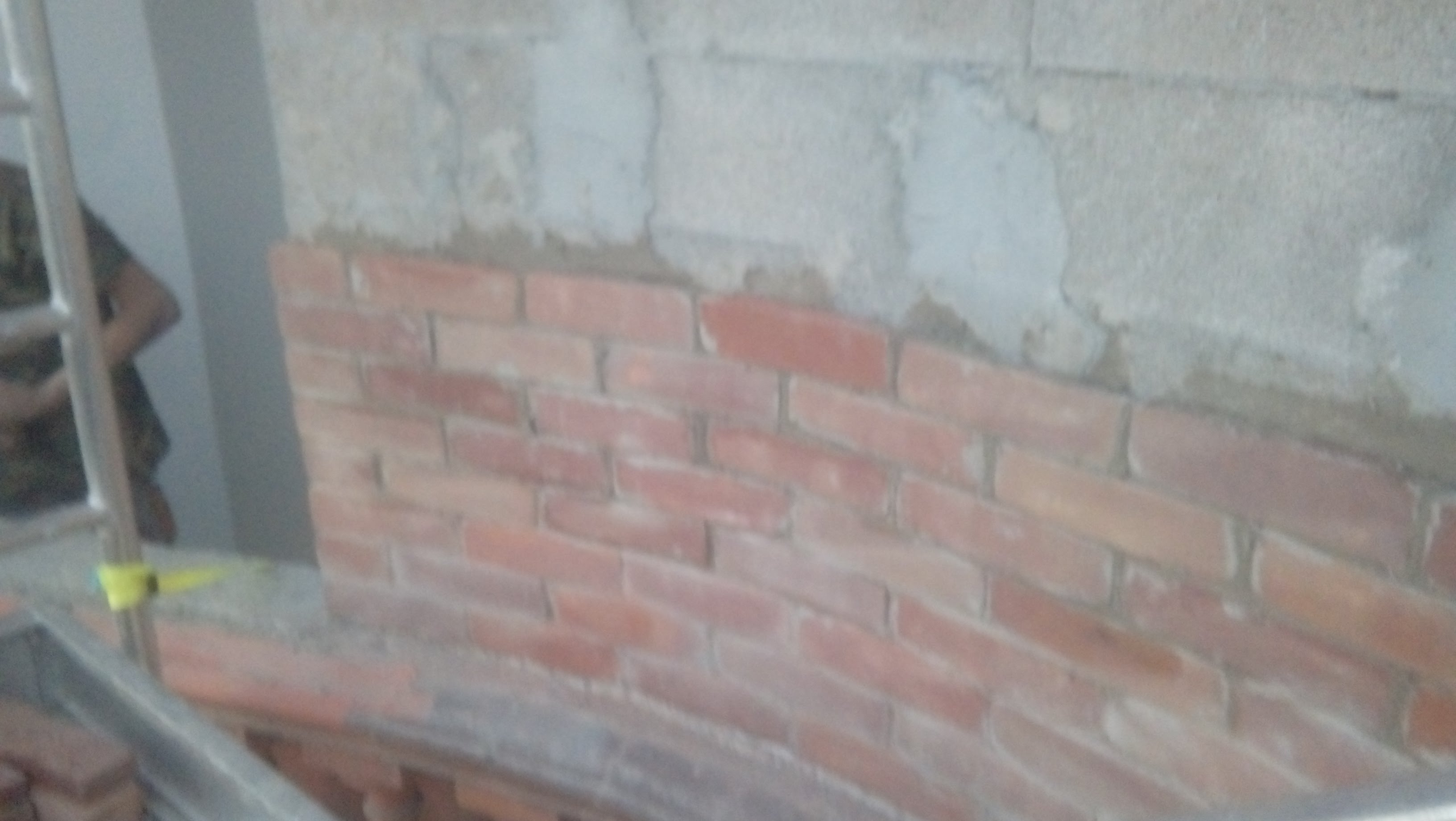 Fragment ściany z nowo położonej cegły licowej, widoczne pozostałości zaprawy na górze ściany i fragment rusztowania.