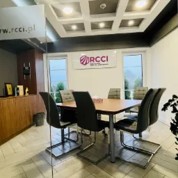 Sala konferencyjna w biurze firmy z Łodzi. W tle widoczne logo firmy budowlanej na ścianie, stół z krzesłami oraz przeszklona ściana z adresem strony internetowej.