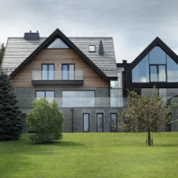 Nowoczesny dom jednorodzinny z dwuspadowym dachem, elewacją z kamienia i drewna, dużymi przeszkleniami i zielonym trawnikiem na pierwszym planie.