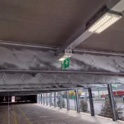 Oświetlenie LED i oznakowanie drogi ewakuacyjnej na parkingu podziemnym w Olesnie, widok z dołu na sufit konstrukcji.