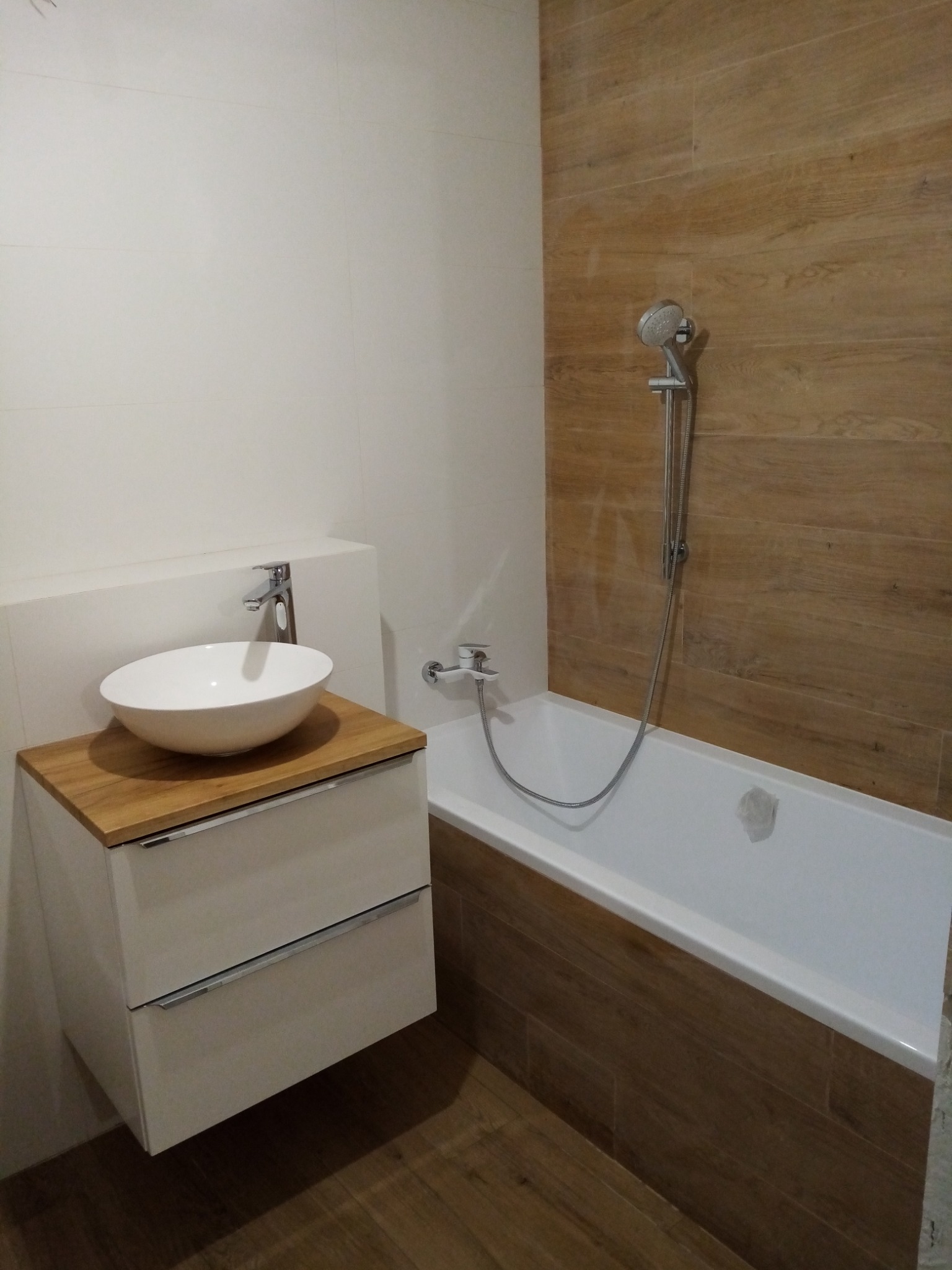 Nowoczesna łazienka z drewnopodobnymi płytkami, białą wanną i umywalką nablatową na szafce z drewnianym blatem.