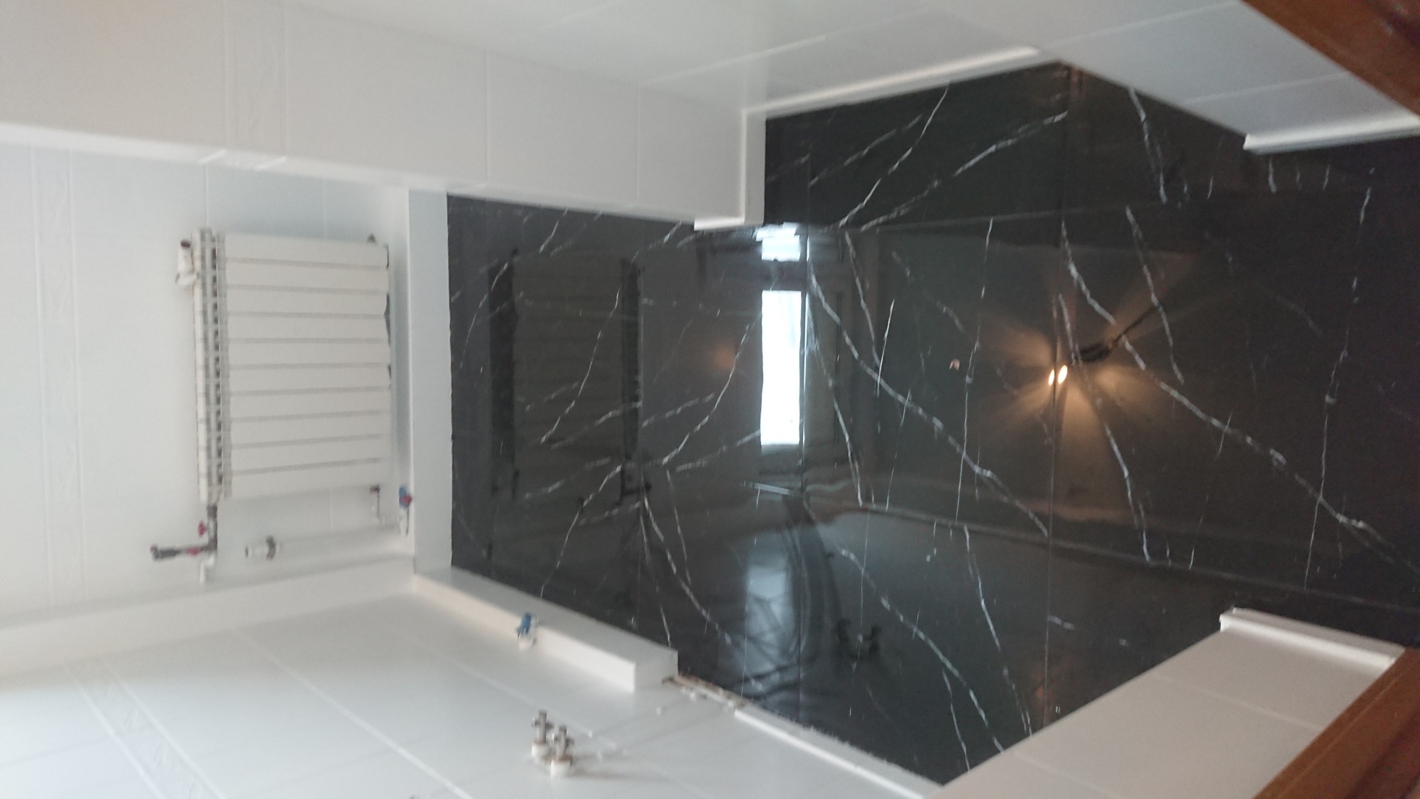 Wykończona łazienka z czarnymi płytkami imitującymi marmur i białym grzejnikiem drabinkowym