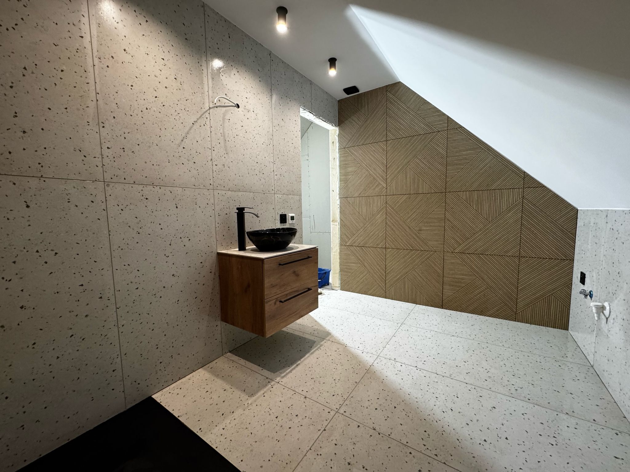 Nowoczesna łazienka na poddaszu z umywalką nablatową, płytkami lastryko na ścianach i podłodze oraz dekoracyjną ścianą z drewnianych paneli.