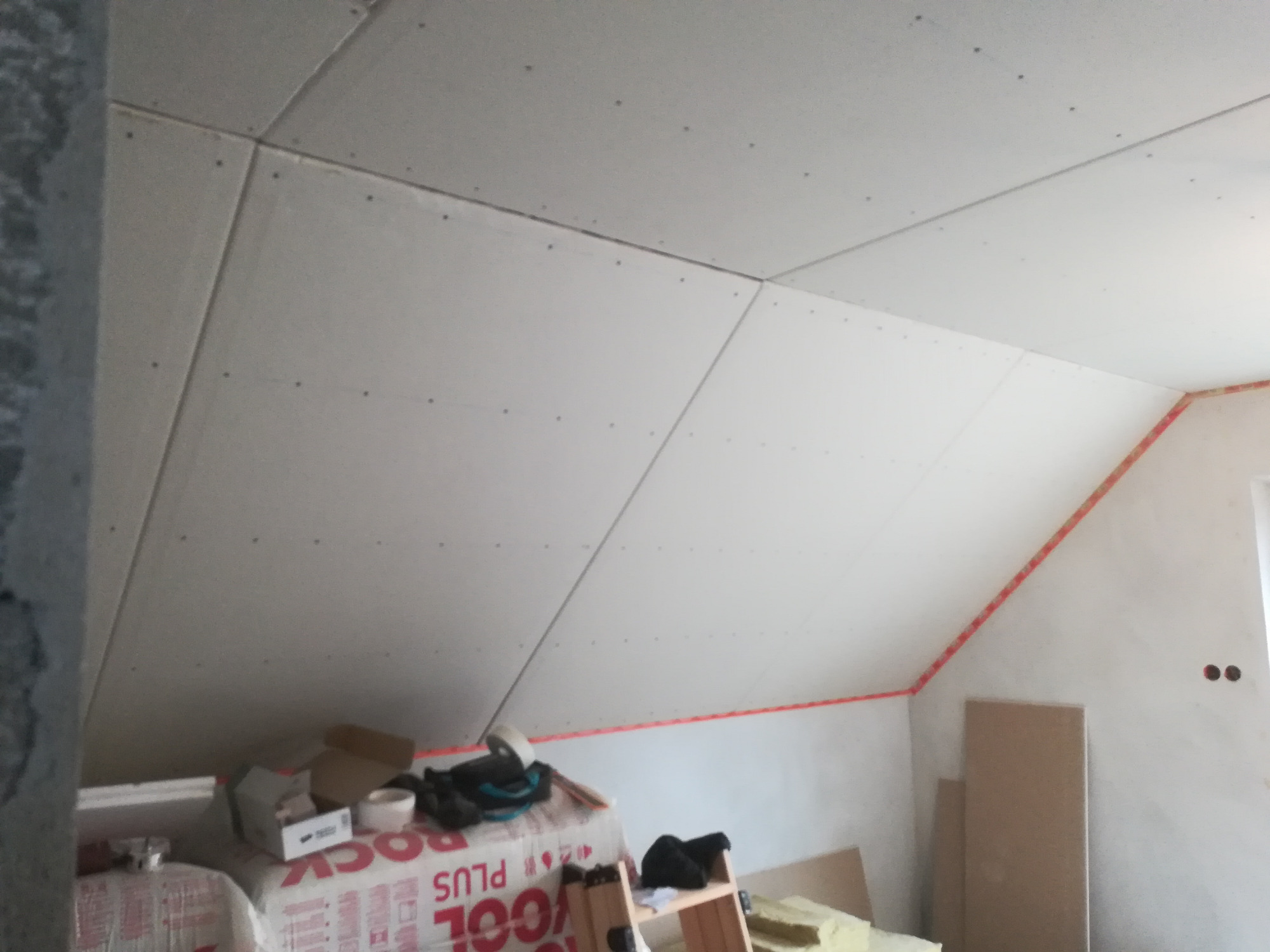 Montaż płyt gipsowo-kartonowych na poddaszu, widoczne wełna mineralna Rockwool Plus i narzędzia pracy.