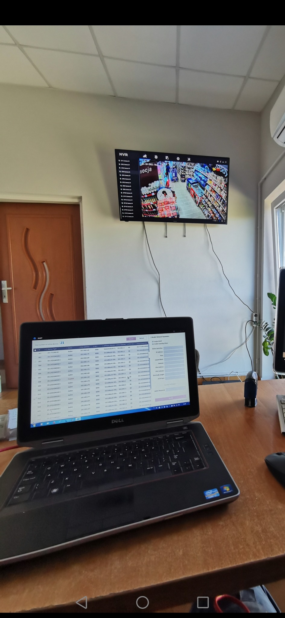 Konfiguracja systemu monitoringu: Laptop z otwartym oprogramowaniem do zarządzania kamerami IP, na ścianie monitor z podglądem z kamer w sklepie.