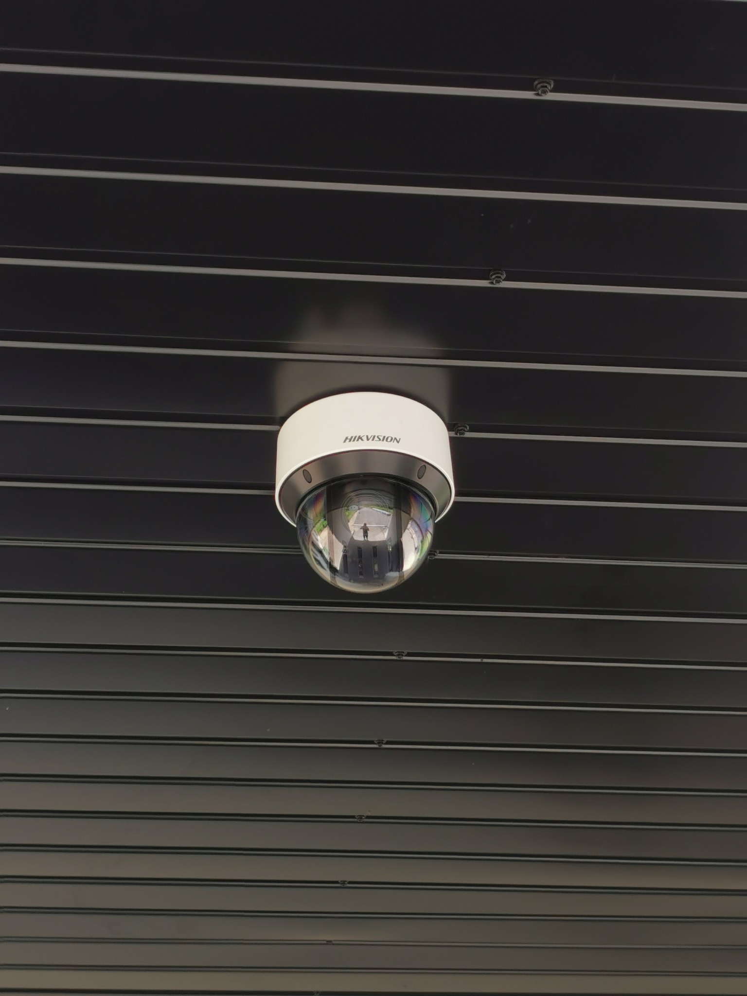 Kamera kopułkowa Hikvision zamontowana na czarnym, poziomym panelu sufitowym.