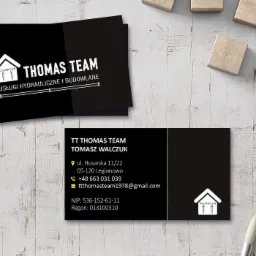 Wizytówki firmy Thomas Team oferującej usługi hydrauliczne i budowlane, leżące na drewnianym blacie obok drewnianych kostek i pędzla.