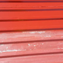 Fragment czerwonego dachu z blachy trapezowej, częściowo odnowionego, z widocznymi śladami starej powłoki i nowym malowaniem w Ostrzeszowie.