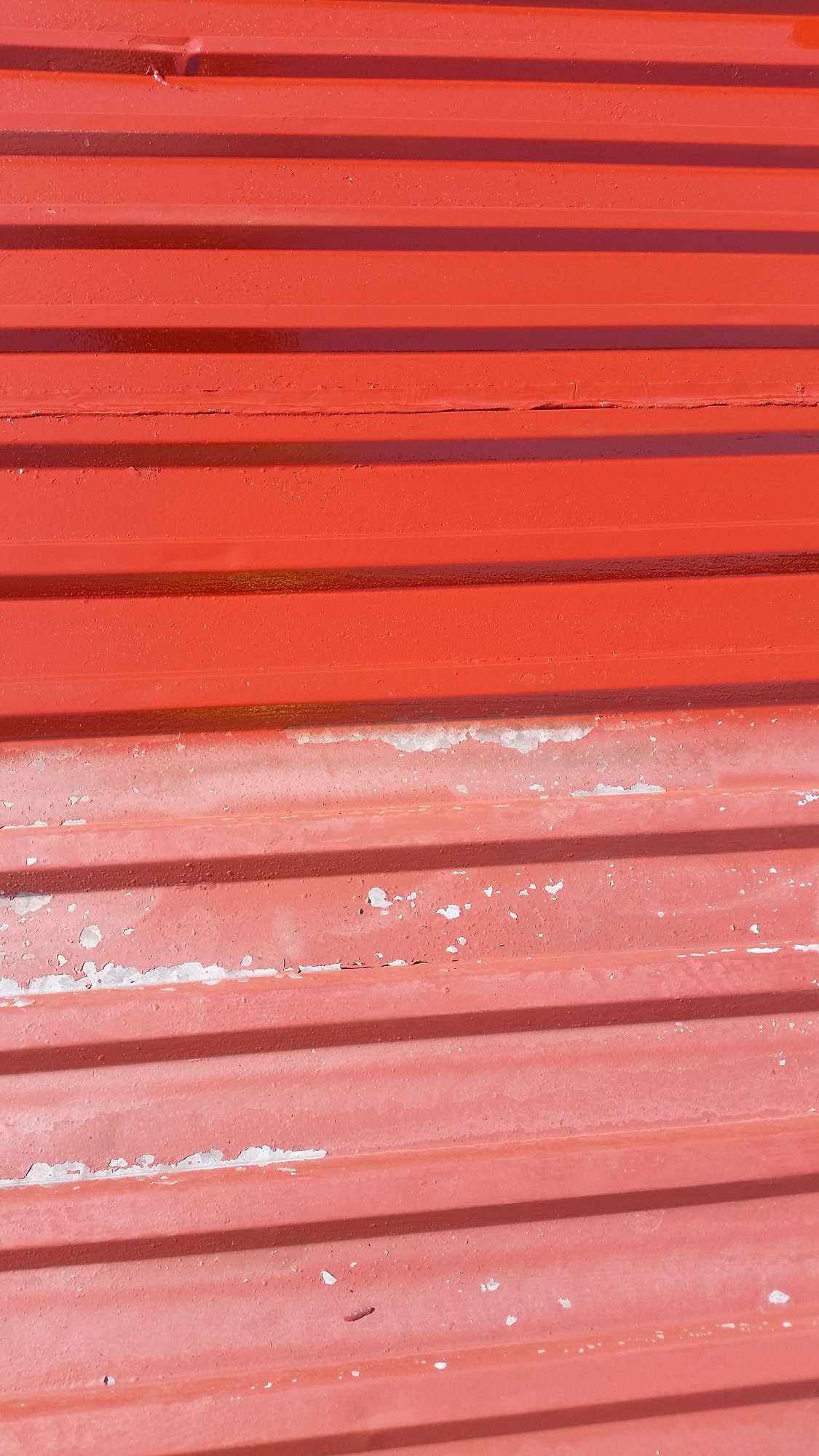 Fragment czerwonego dachu z blachy trapezowej, częściowo odnowionego, z widocznymi śladami starej powłoki i nowym malowaniem w Ostrzeszowie.