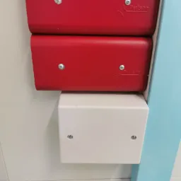 Dwa czerwone moduły Pulsar z widocznymi śrubami montażowymi, umieszczone nad białą skrzynką elektryczną, całość zamontowana na jasnej ścianie z niebieskim elementem konstrukcyjnym z prawej strony.