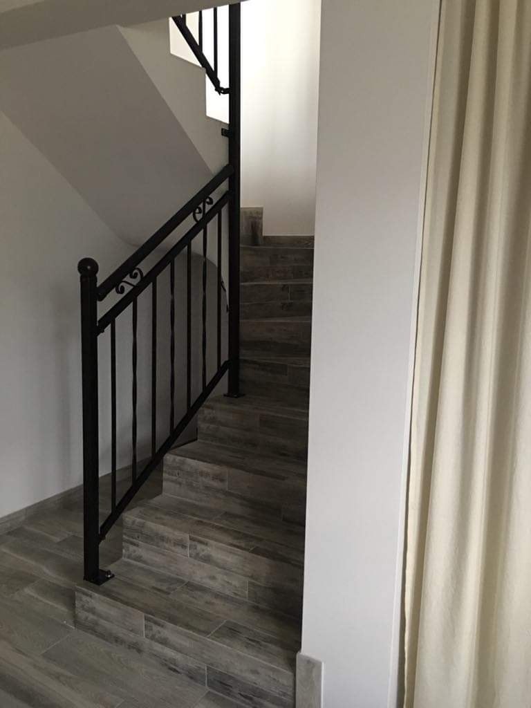 Schody wyłożone płytkami imitującymi drewno, z czarną, metalową balustradą i kremową zasłoną w tle.