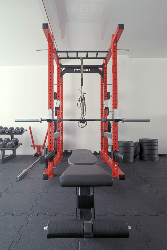 Czerwona klatka do ćwiczeń z czarną ławką i obciążeniami w domowej siłowni z podłogą z puzzli gumowych.