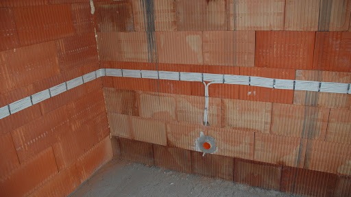Instalacja elektryczna w nowym budynku: przewody ułożone w korytkach na ścianie z czerwonej cegły, widoczne puszki instalacyjne.