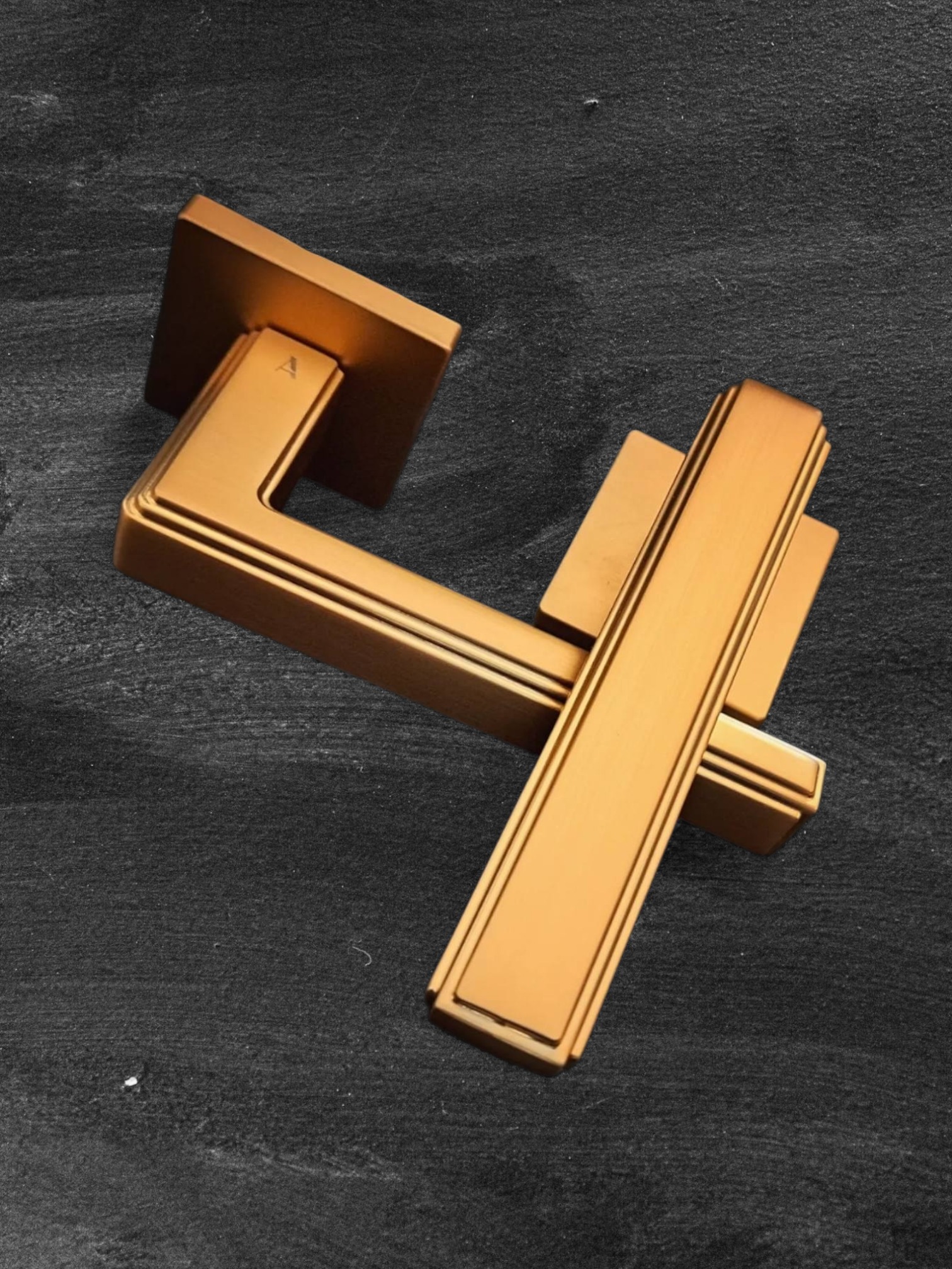 Złoty, kwadratowy uchwyt do drzwi wewnętrznych z delikatnymi żłobieniami, leżący na ciemnym, teksturowanym tle. Minimalistyczny design, ciepłe oświetlenie.