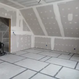 Poddasze w trakcie wykańczania: ściany i skosy obłożone płytami kartonowo-gipsowymi, szpachlowane łączenia, widoczne fragmenty instalacji elektrycznej, przygotowana podłoga z zaznaczonym układem...