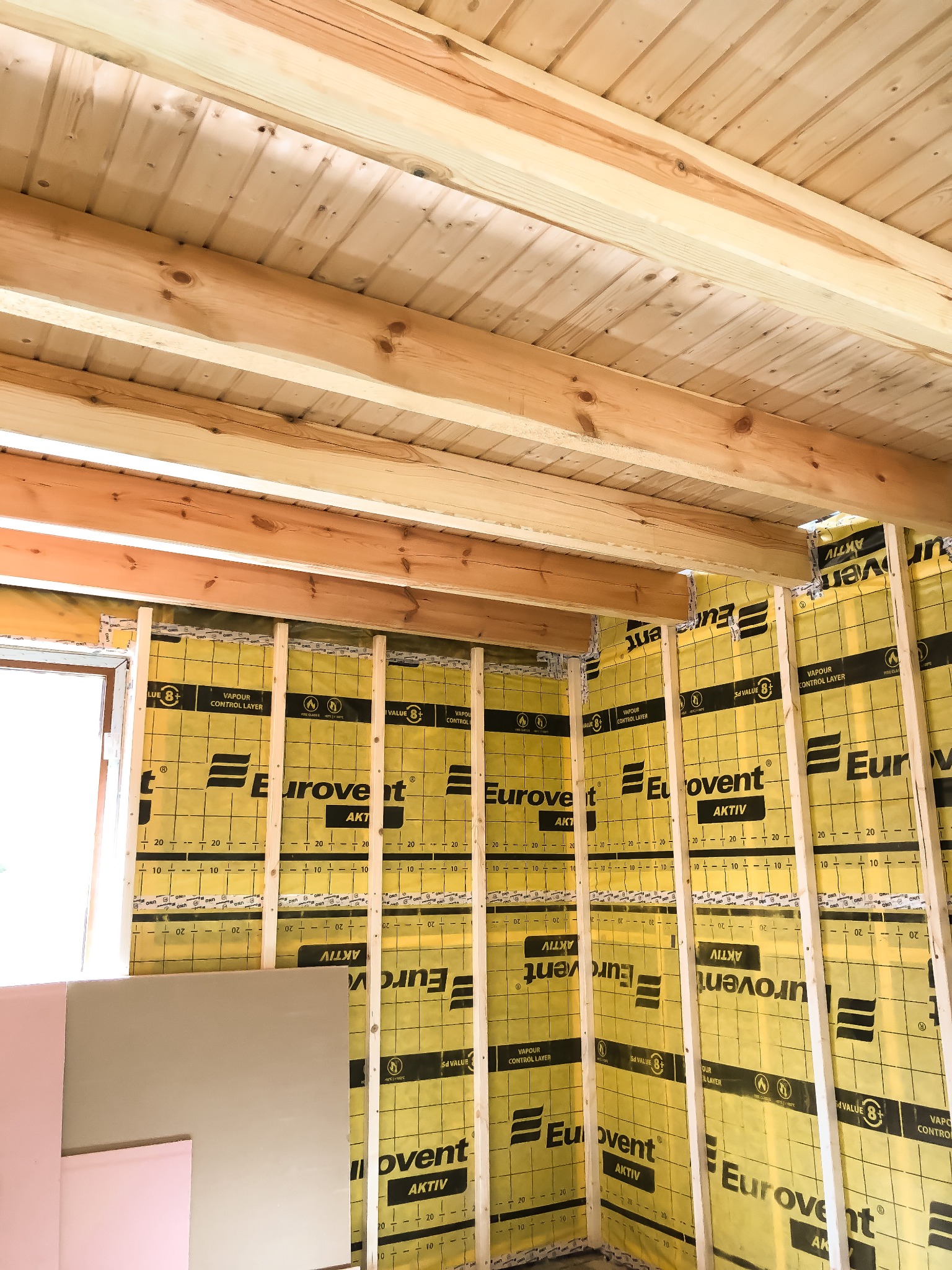 Wnętrze w trakcie budowy domu szkieletowego: widoczne drewniane belki stropowe, ściany z izolacją Eurovent Aktiv i fragment płyty gipsowo-kartonowej.
