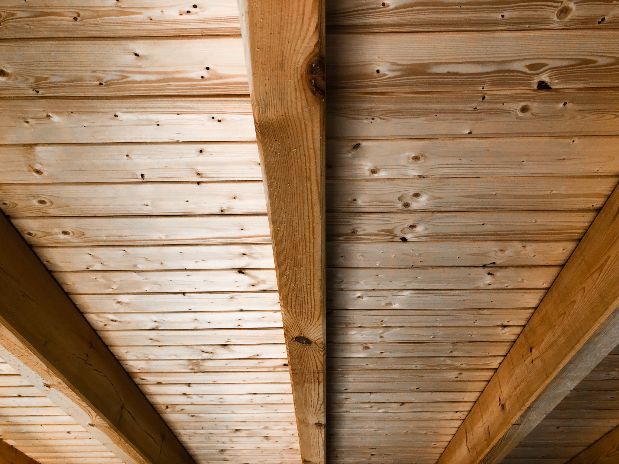 Widok od dołu na drewnianą konstrukcję dachu z widocznymi belkami i deskami, naturalne drewno z sękami i przebarwieniami.