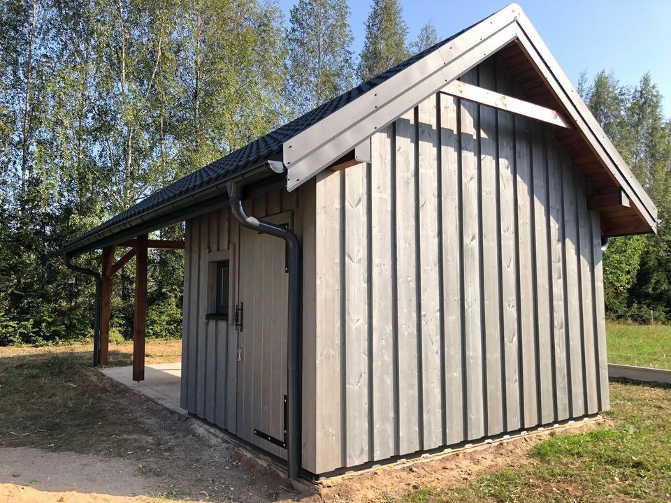 Gotowy, szary budynek gospodarczy z drewnianą elewacją pionową i czarnym dachem, z widocznym systemem rynnowym, na betonowej wylewce.