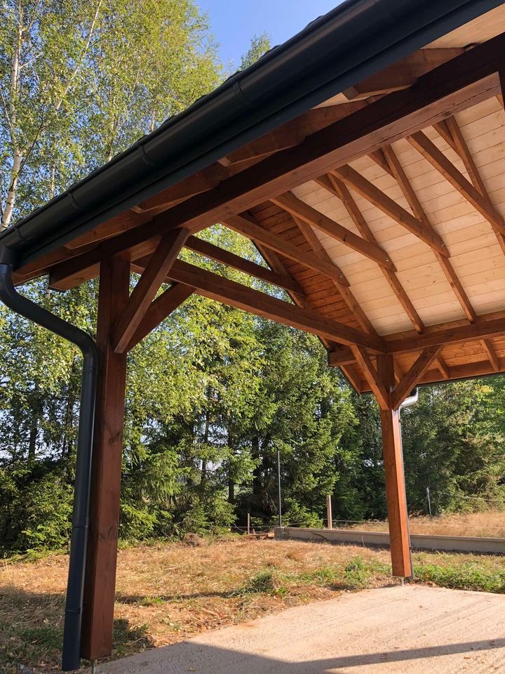 Drewniana konstrukcja z dachem i rynnami, widok z dołu na tle zieleni drzew i trawy.