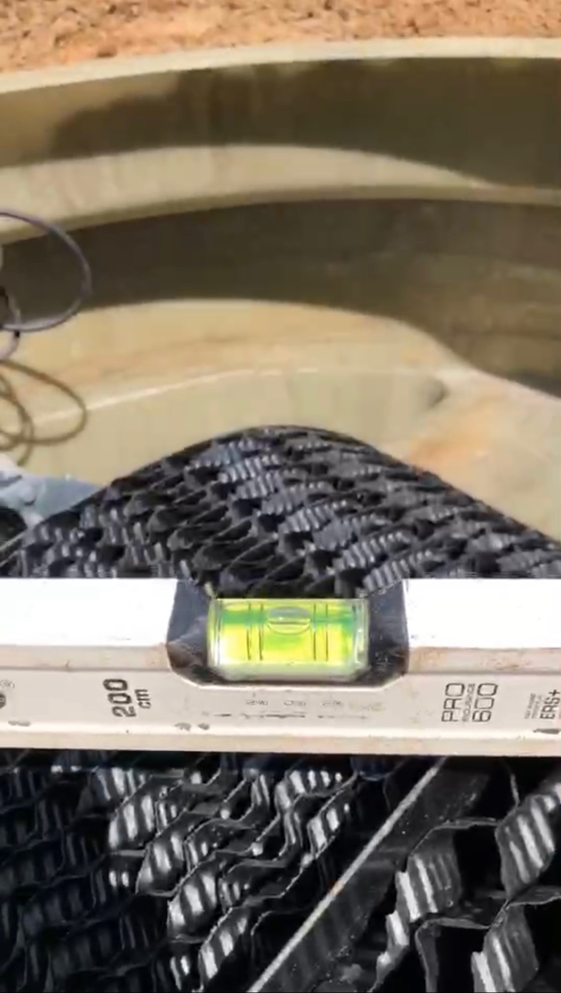 Wnętrze zbiornika z wkładem biologicznym, poziomowany poziomicą. Widoczne elementy instalacji i fragment zbiornika z tworzywa.