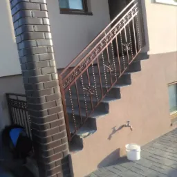 Montaż kutej balustrady schodowej w Żelechlinku, widoczne narzędzia i pracownik przy kolumnie z cegły klinkierowej.