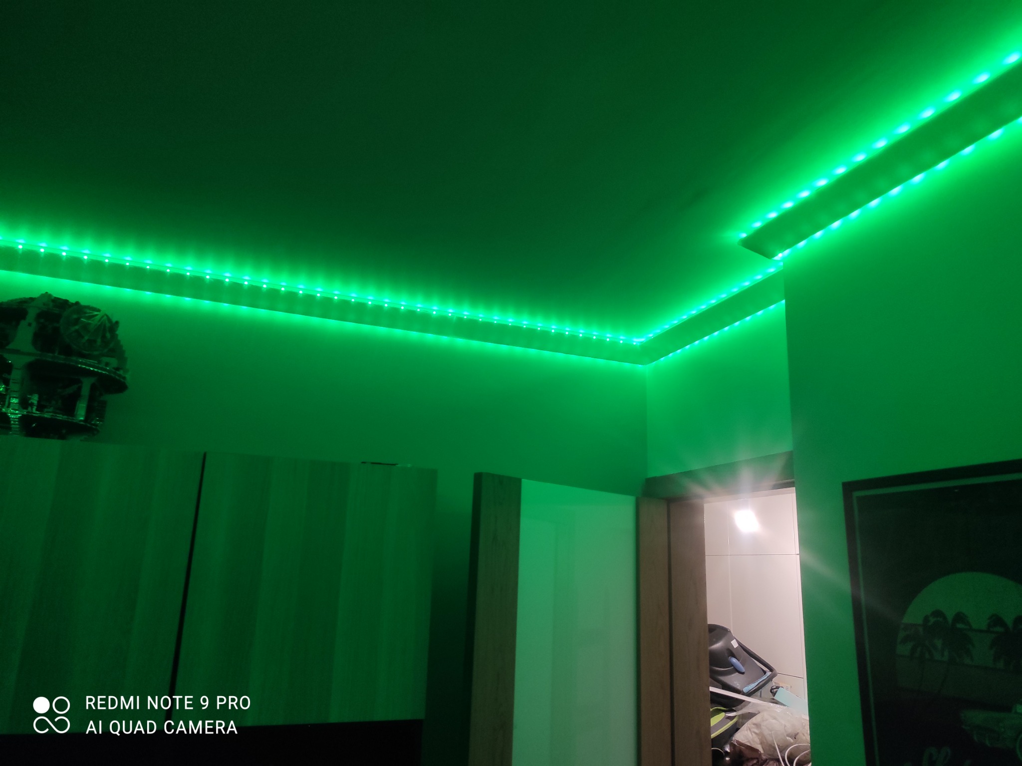 Pokój z zielonym oświetleniem LED na suficie, widoczne fragmenty mebli i dekoracji, tworzące nowoczesny, klimatyczny wystrój wnętrza.