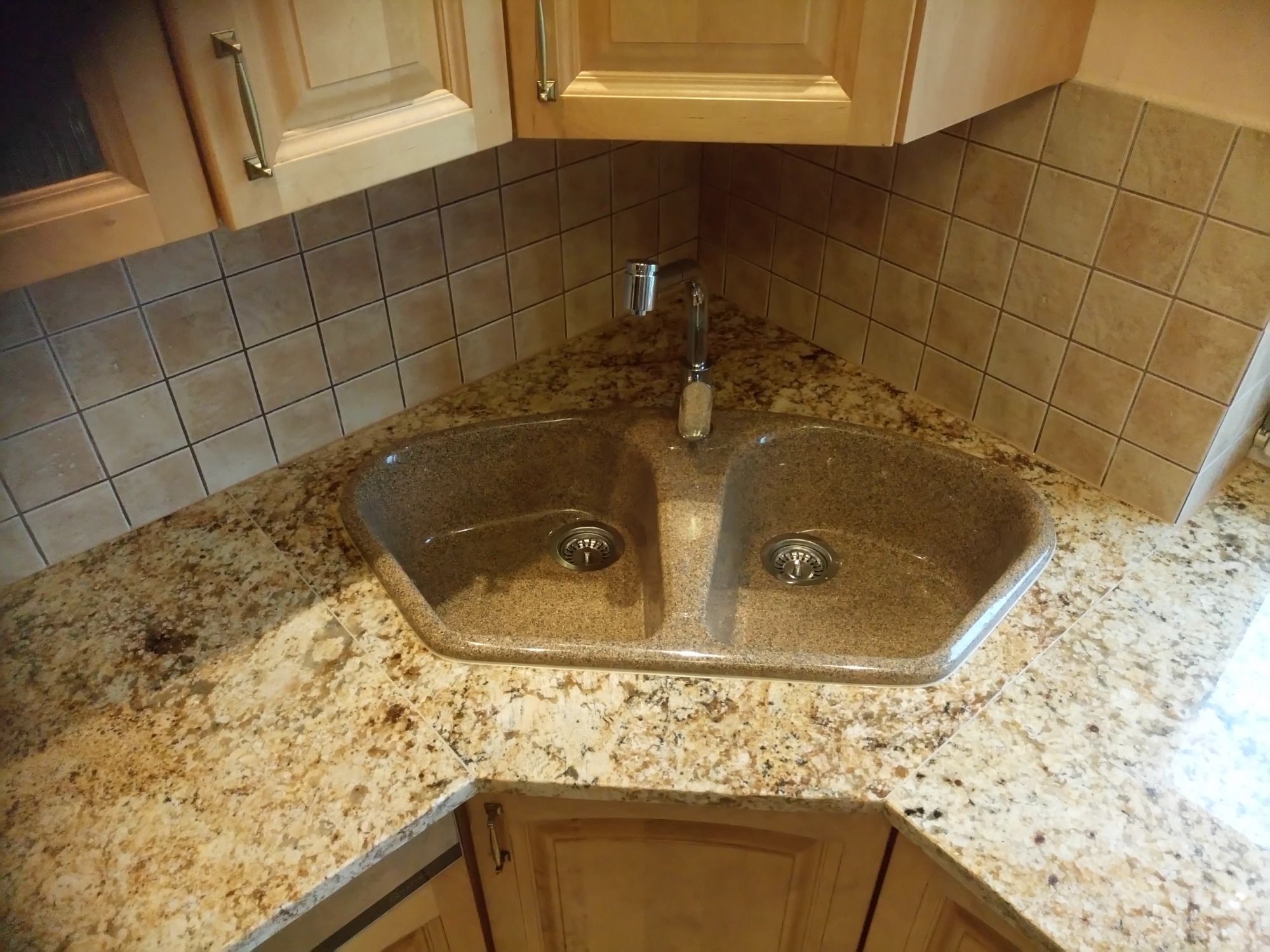 Granitowy blat kuchenny w odcieniach beżu i brązu z wpuszczonym dwukomorowym zlewozmywakiem, dopasowany kolorystycznie do blatu, oraz chromowaną baterią, całość w narożniku kuchni wykończonym...