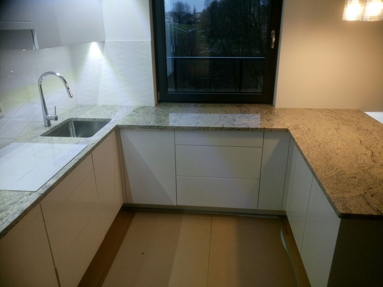 Kuchnia z blatem z granitu Colonial Ivory, widoczny zlew, płyta indukcyjna i okno z widokiem na zieleń.