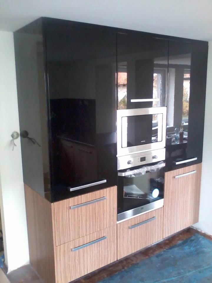 Część zabudowy kuchennej z czarnymi, błyszczącymi szafkami górnymi i drewnopodobnymi szafkami dolnymi, z wbudowanym piekarnikiem i mikrofalówką.